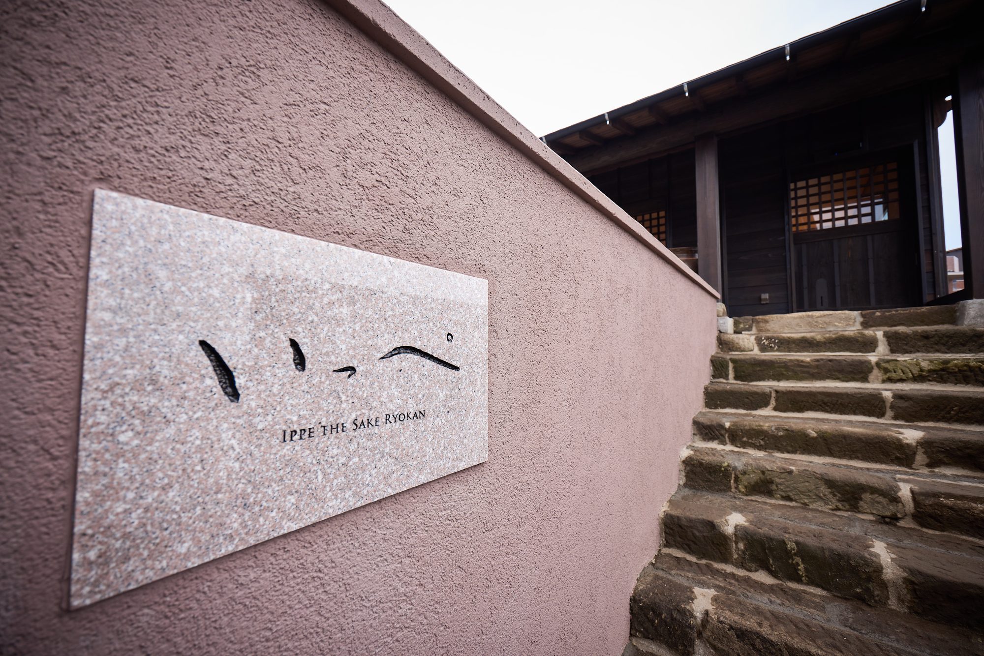 石段の脇に掲げられた いっぺ THE SAKE RYOKAN の看板
